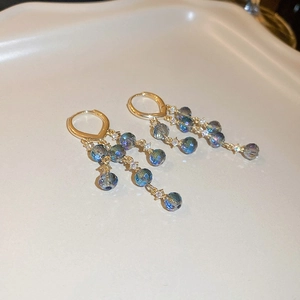 Detail of gold huggie earrings with layered blue beads and rhinestone tassel fringe