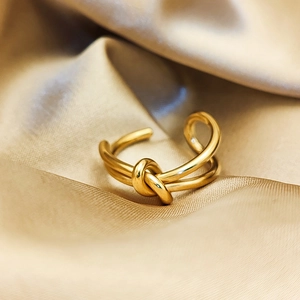 Detailed close-up of a 14K gold plated knot ring on soft champagne silk fabric