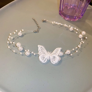 Détail d'un ras de cou en perles avec broderie papillon en dentelle sur plateau gris