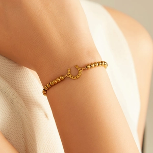 Detail of 18K gold plated bead bracelet with horseshoe pendant on female wrist
