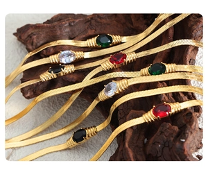 Macro shot of gold snake chain with colorful oval gemstones on a textured wood block