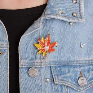 Detailed close-up of a gradient maple leaf brooch with an elegant pearl on denim jacket
