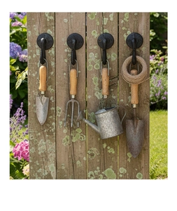 Close-up of vintage black cast iron wall hooks holding garden tools on wooden fence