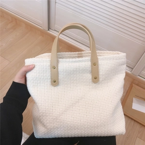 Detail of white woven tote bag with beige leather handles and metallic rivet fixings