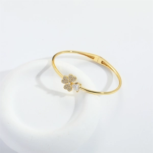 Detail of gold open bangle with clover and heart charms set in sparkling zircons