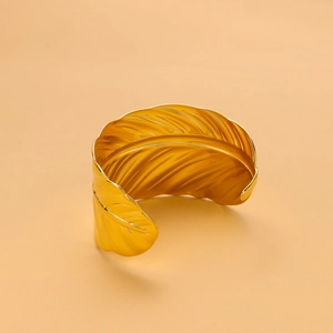 Detailed view of an elegant gold leaf-shaped stainless steel cuff bracelet on beige