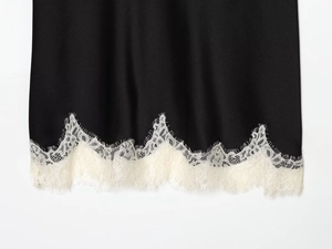 Close-up of black satin fabric with intricate white eyelash lace trim at the bottom hem