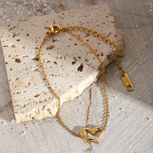 Bracelet en acier inoxydable doré avec pendentif cœur sur fond de pierre beige