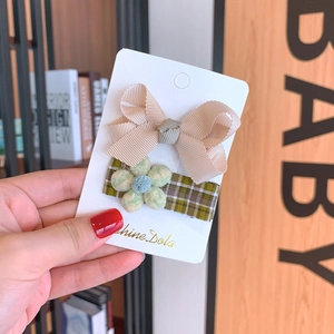 Detail showing soft beige ribbon bow and green plaid hair clip with knitted flowers