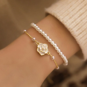 Detail of layered gold-plated chain bracelet with white camellia flower and pearls