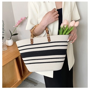 Detail of hand-woven straw tote bag with black and white stripes and bamboo handles