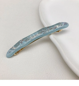 Dettaglio del fermaglio per capelli ondulato azzurro traslucido con glitter e base dorata