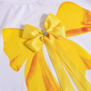 Détail d'un nœud papillon 3D jaune avec strass sur un haut blanc à imprimé papillon