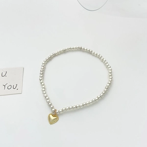 Detailed close-up of beaded silver bracelet featuring a golden heart pendant