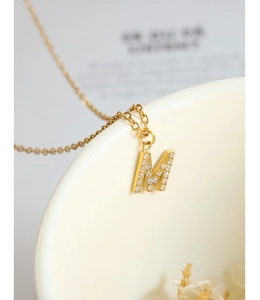 Macro shot of gold M-letter pendant with sparkling zircons on a white ceramic cup