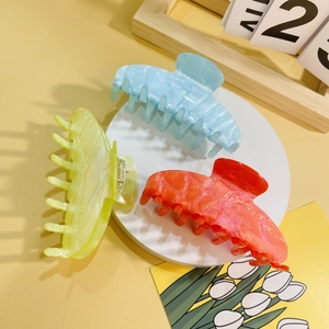 Close-up of three large glittery acrylic hair claws in blue, yellow and orange colors