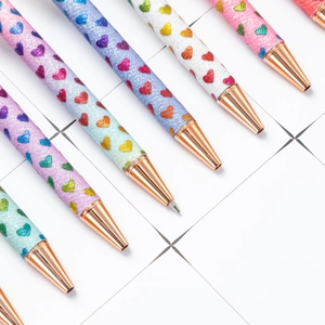Glitter ballpoint pens with heart patterns and rose gold metal clips on white background