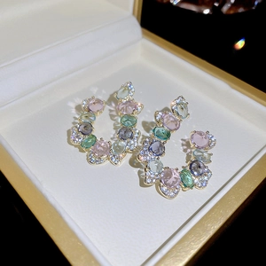 Macro view of C-shaped earrings with colorful gemstones and pavé crystals in a jewelry box