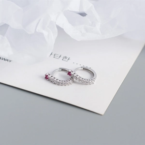 Macro shot of S925 sterling silver hoop earrings with clear diamonds and a red gemstone