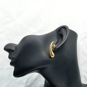 Detail of gold teardrop earrings worn on a black model head with a stylish fluid design