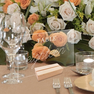 Clear acrylic wedding table number eighteen with natural wooden base on a floral table