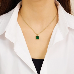 Close-up of golden necklace featuring an emerald green rectangular gemstone pendant