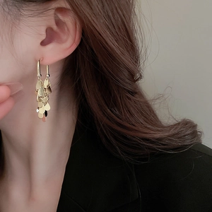 Detailed close-up of golden sequin tassel earrings worn by a model with metal texture