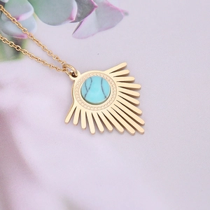 Golden sunburst pendant necklace with turquoise stone on soft pink fabric background