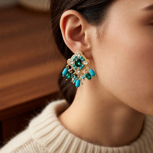 Close-up of vintage drop earrings with green stones and blue beads on a model wearing a sweater