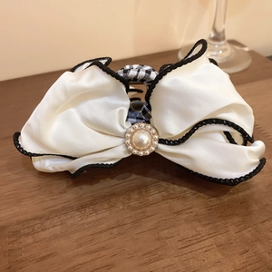 Detail of white satin bow hair claw clip with pearl accent and checkerboard pattern