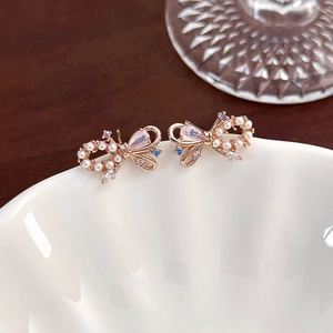 Macro detail of rose gold bow earrings with colorful zircon stones and white pearls