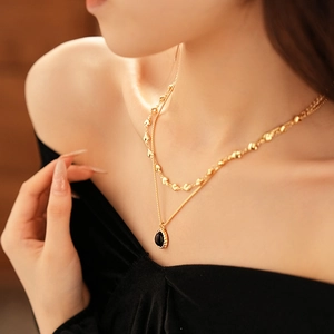 Detail of double-layer gold necklace with heart chain and black oval pendant on neck