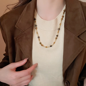 Gros plan du collier de perles œil de tigre vintage porté avec une tenue de style Maillard