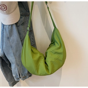 Detail of green nylon dumpling bag with pleated texture hanging next to denim jacket