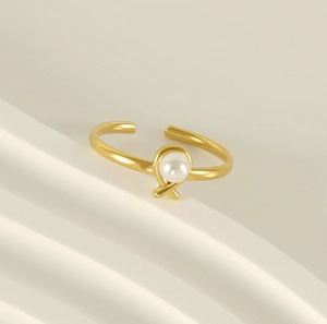 Close-up of golden pearl ring with knot design on white geometric display stand