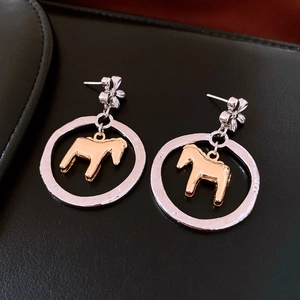 Detailed top-down view of Dala horse earrings on black leather with gold and silver finish