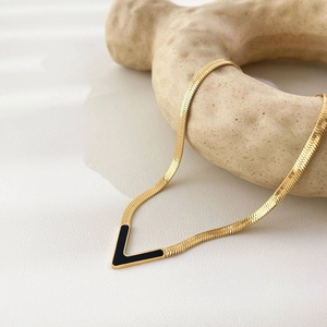 18K gold plated titanium V-shaped necklace on beige display stand with black pendant