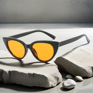 Detail of retro cat-eye sunglasses with black frames and bright orange lenses on stone