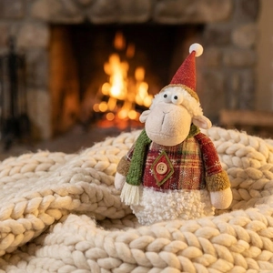 Close-up of sheep plush toy with red plaid details on a cozy knit blanket by fireplace