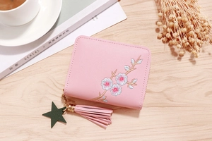 Pink PU leather wallet with floral embroidery, gold zipper, and tassel on wooden table