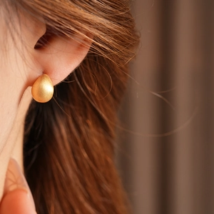 Close-up of matte gold-plated teardrop earrings showing minimalist metallic texture
