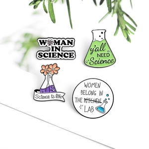 Flat lay of four science enamel pins with green leaves on a clean white background