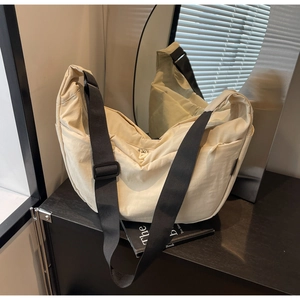 Minimalist beige nylon dumpling bag with adjustable wide black shoulder strap detail