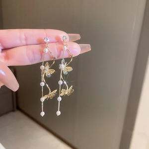 Detail of gold butterfly tassel earrings with faux pearls and sparkling crystal accents