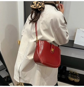 Detail of red patent leather saddle bag with gold buckle on a model's shoulder