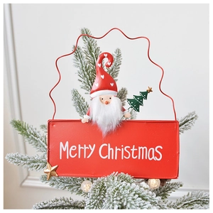 Detail of red metal Merry Christmas sign with a cute gnome hanging on snowy pine tree