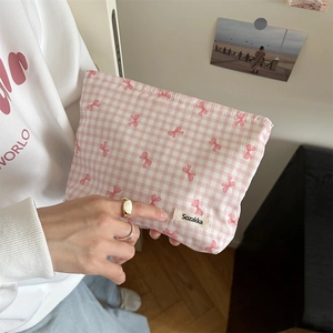 Detail view of pink plaid makeup bag with bow patterns held by a hand showing soft fabric