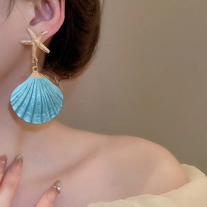 Detailed view of starfish stud earrings with blue shell pendants on model for vacation look