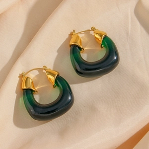 Dettaglio di orecchini placcati oro con acrilico verde trasparente su seta beige