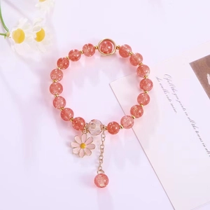 Detailed view of pink strawberry crystal bracelet with daisy charm and gold tassels